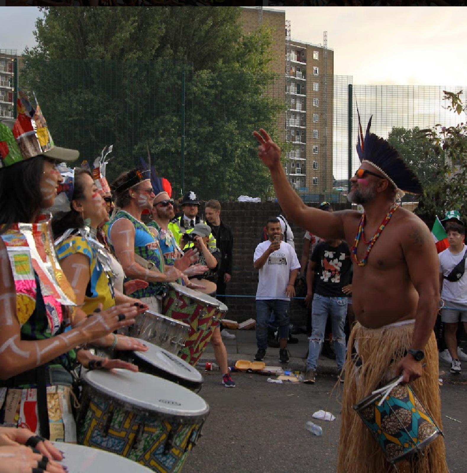 TRIBO musical director in a feathered headdress raising his hand while leading drummers at Notting Hill Carnival
