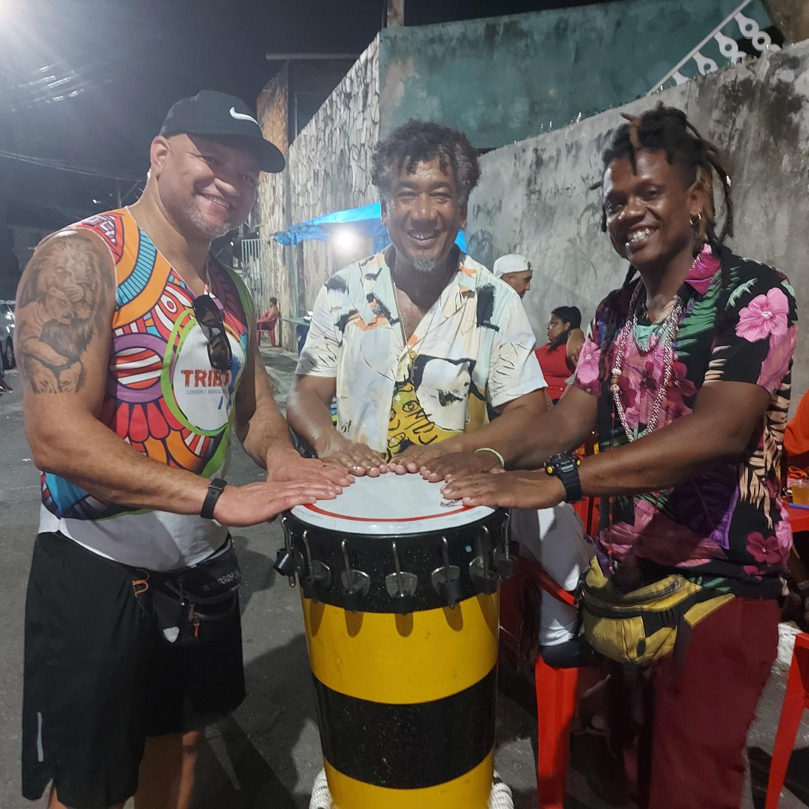 Marcos Santana with two Bahian master percussionists resting their hands together on a timbau at night