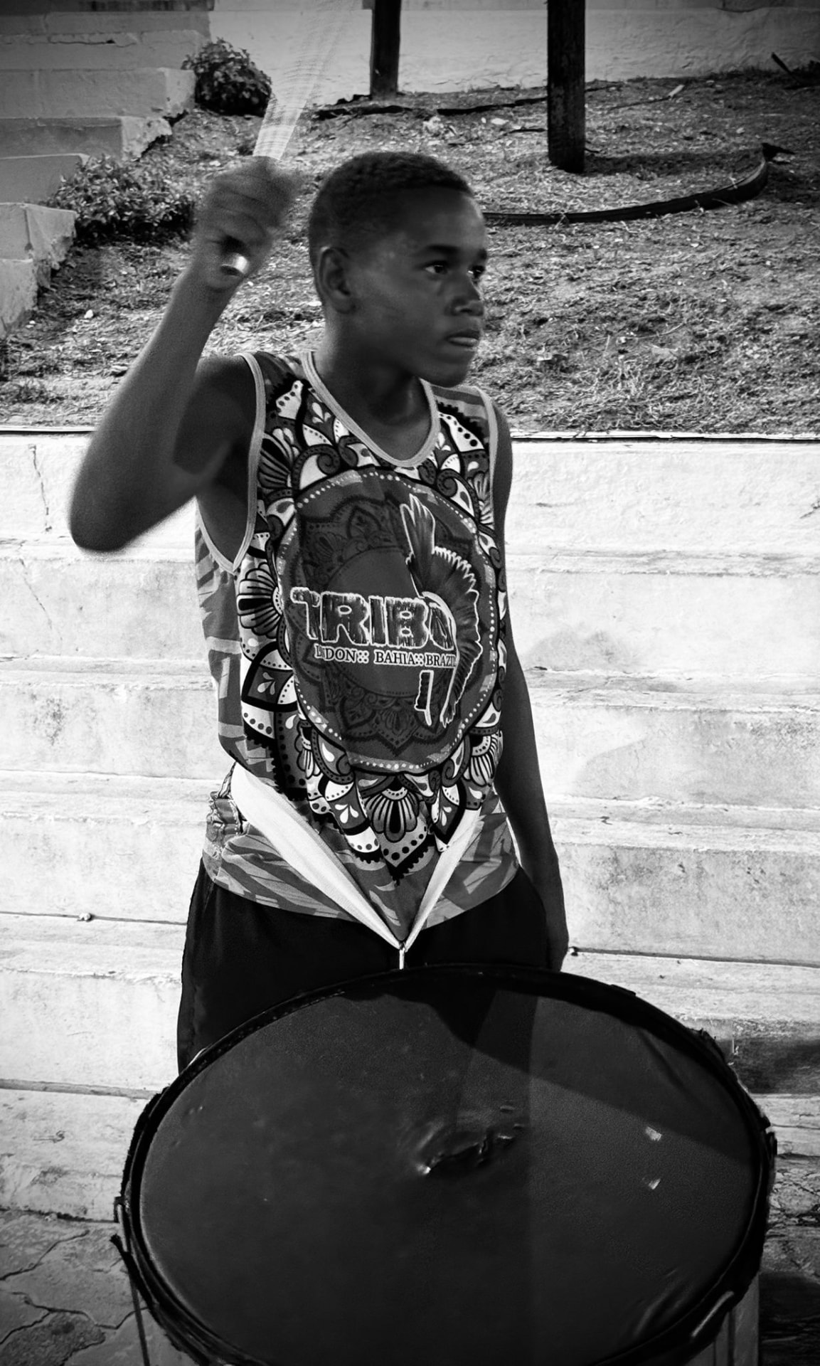 Black and white photograph of a young TRIBO student raising a drumstick above a surdo
