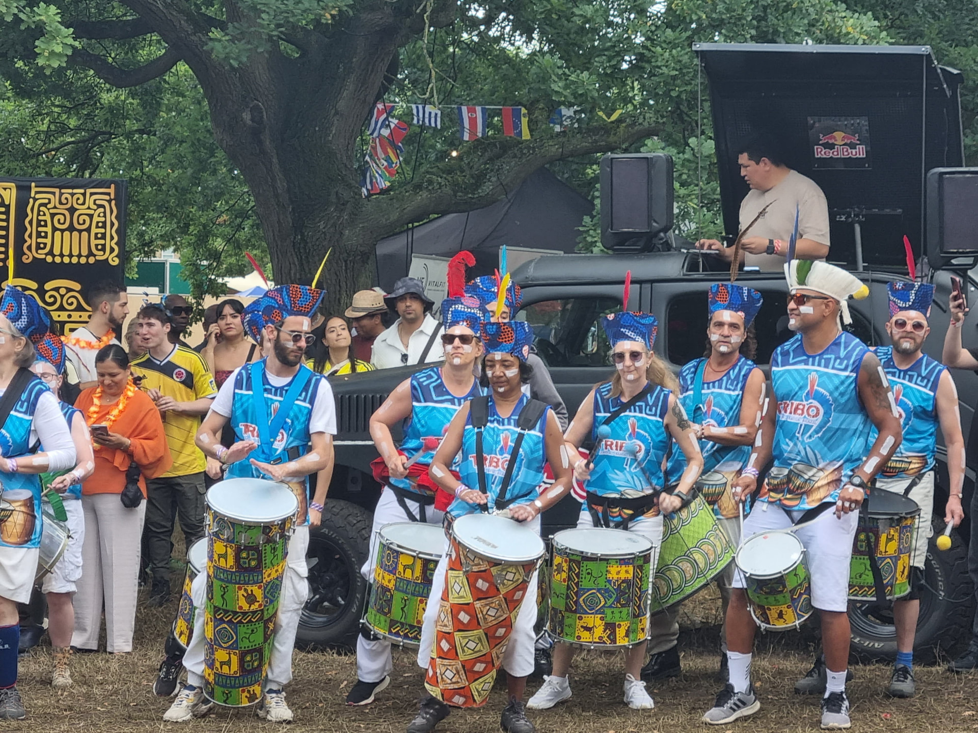 Wide view of the TRIBO bloco in blue vests playing surdos and caixas in front of a festival sound truck in London