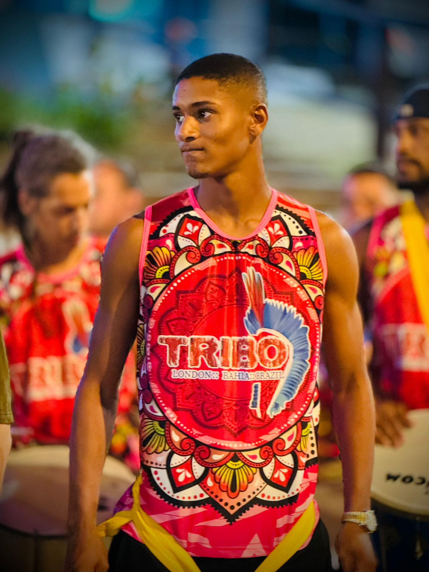 Portrait of a young TRIBO drummer wearing the red TRIBO London Bahia Brazil vest at night
