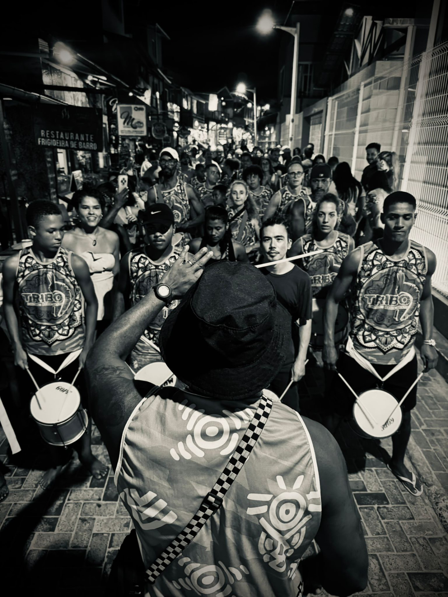 Black and white photograph of a TRIBO director conducting the bloco in a busy Bahian street at night