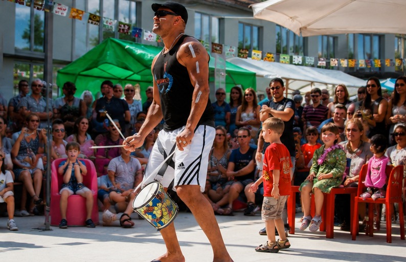 TRIBO percussionist performing with a snare drum in front of a seated crowd at an outdoor event