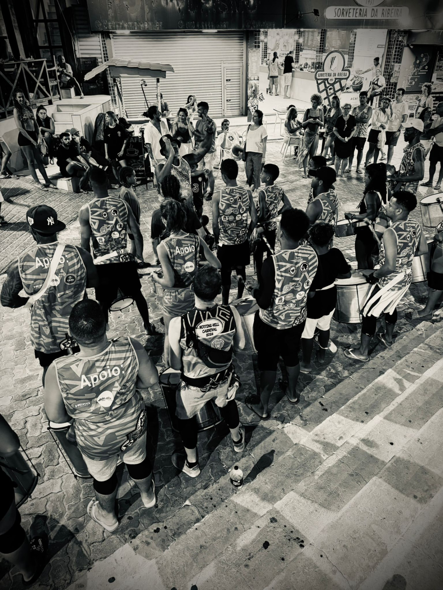 Aerial view of the TRIBO bloco rehearsing in a circle in a square in Ribeira, Salvador, surrounded by onlookers