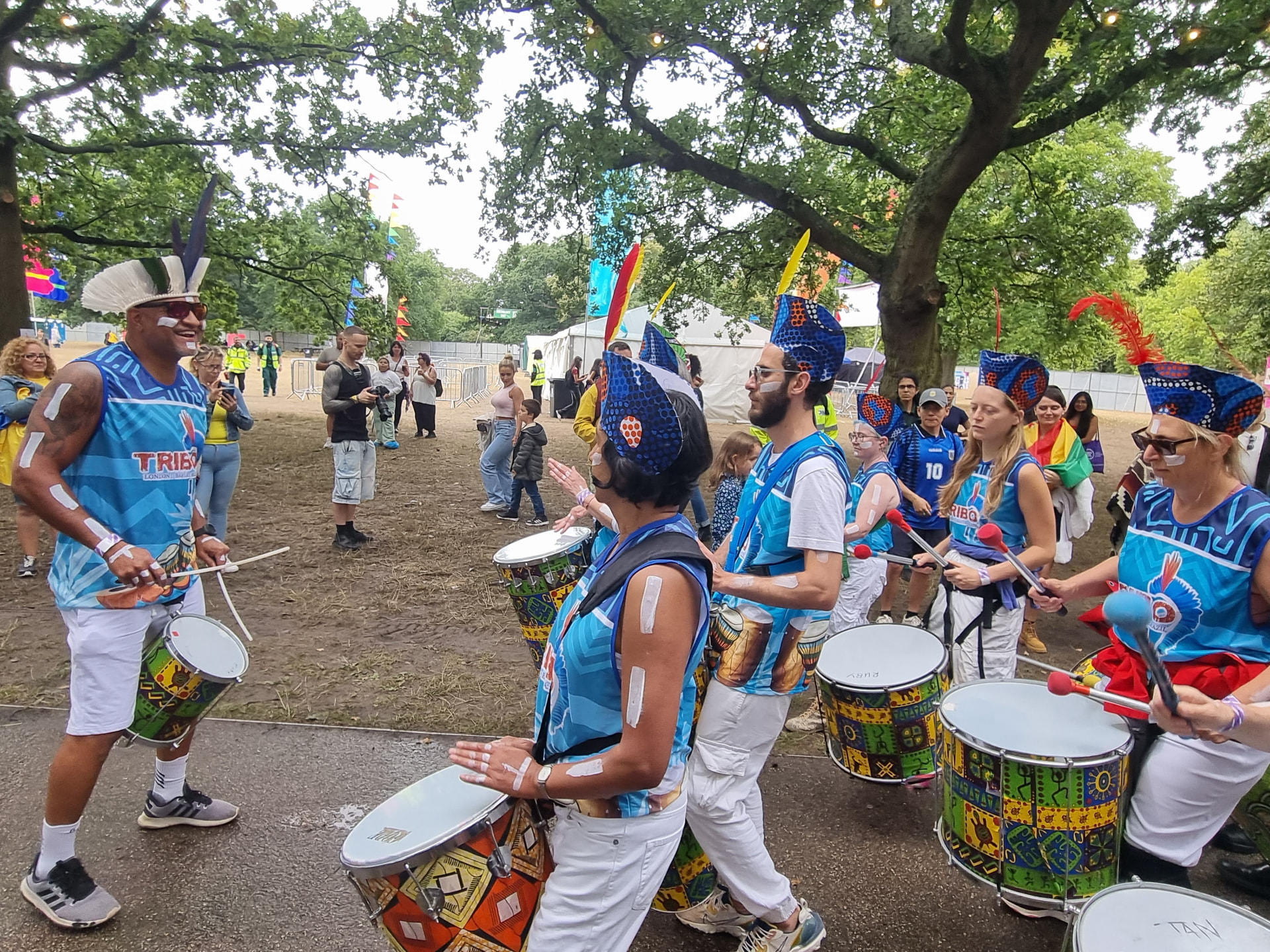 TRIBO musical director in a white feathered headdress leading the drummers at a London festival