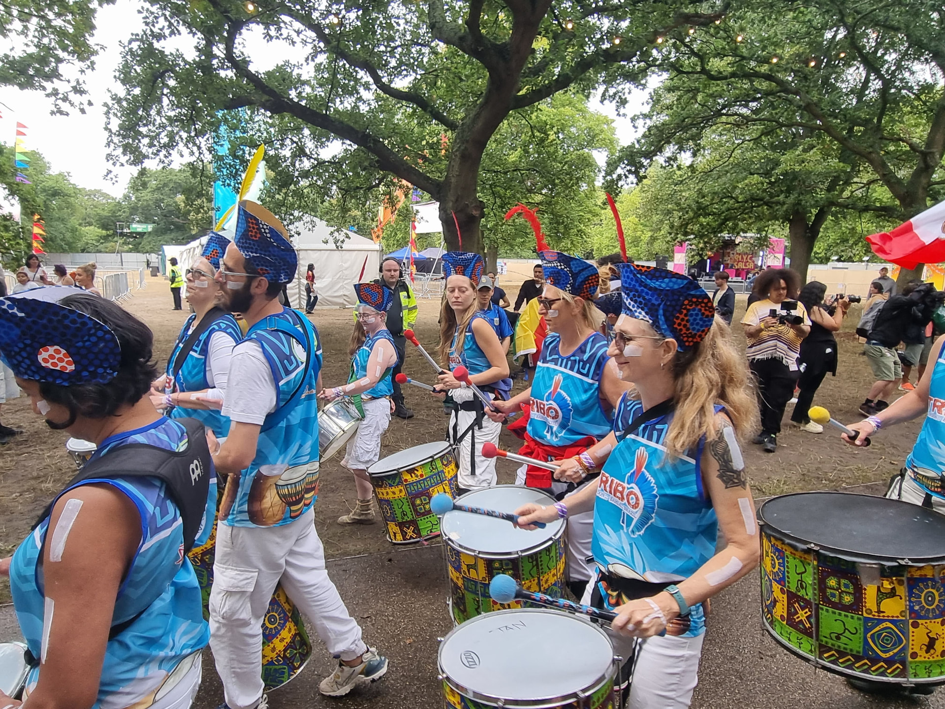TRIBO drummers marching along a path at a London festival with flags and crowds behind them