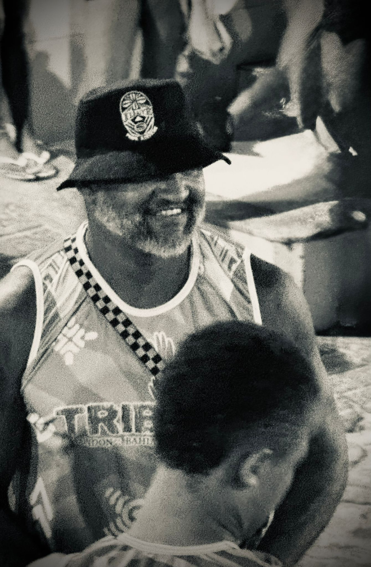 Smiling elder member of TRIBO in a bucket hat and band vest during an outdoor rehearsal